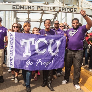  A group Ӱɴý students walks across the Edmund Pettus Bridge in Selma, Alabama. They hold a Ӱɴý flag and several students make the wo-fingered Go Frogs hand gesture.