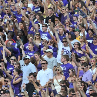 Dozens of cheering Ӱɴý fans raise their arm in a two-fingered "Go Frogs" hand sign at a crowded football game.
