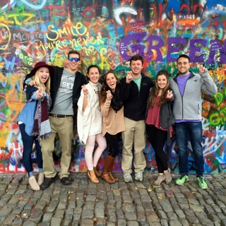 Seven Ӱɴý students studying abroad stand in front of a brightly spray-painted graffitti wall on a cobblestone street in Prague.