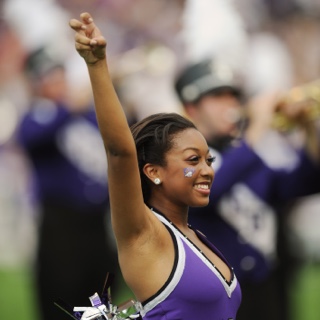 A smiling Ӱɴý Showgirl makes the two-fingered "Go Frogs" hand sign at a crowded football game.