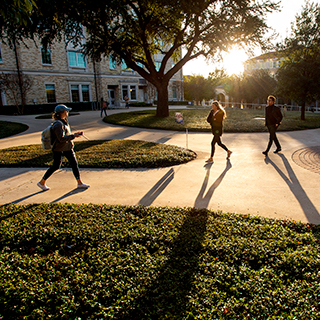 Ӱɴý students wearing jackets walk on campus, casting long shadows on a sunny day
