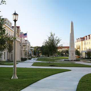Exterior of the Greek Village at Ӱɴý, where a tall obelisk monument bearing greek letters is surrounded group of sorority and fraternity houses 