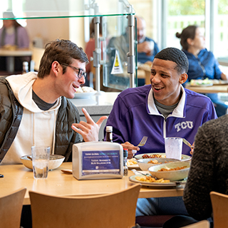 Two male Ӱɴý students share a laugh over lunch at the campus main dining hall