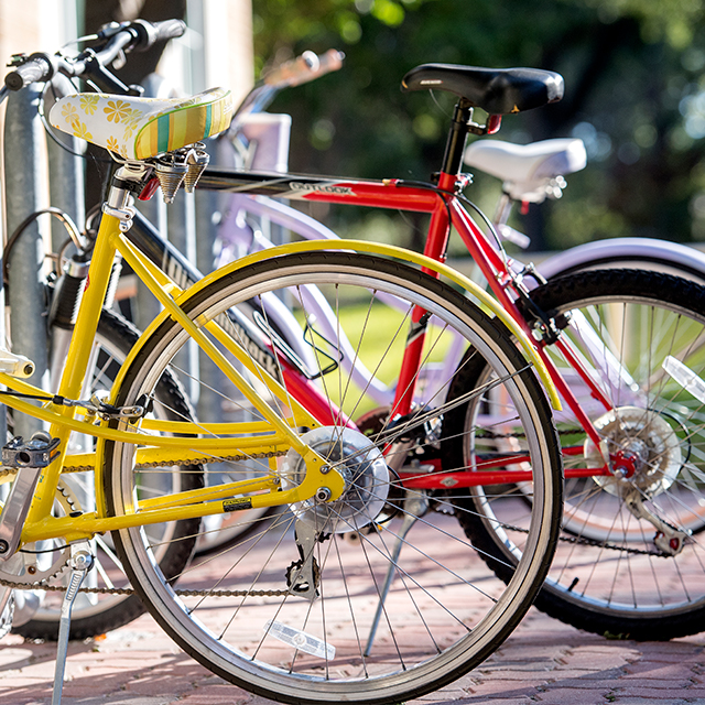 Close up of a bicycle rack on the Ӱɴý campus with pink, red, and yellow bikes