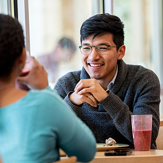 A young male student wearing glasses smiles across a table at a young woman in Market Square, the main Ӱɴý dining hall.