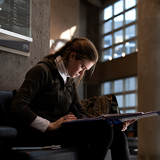 A young women sits alone and looks down intently at her book in the sunlit lobby of Ӱɴý's Moudy Hall North.