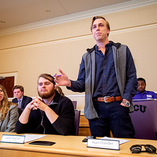 A male student stands to speak at a Ӱɴý student government meeting in the chambers of the student union.
