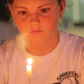 Close up of female Ӱɴý student looking thoughtful as she holds a candle before her face.